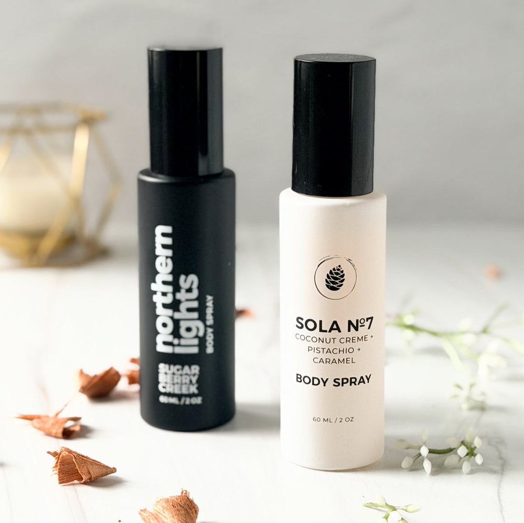Black and white body spray bottles on a white surface with a gold candle in the background