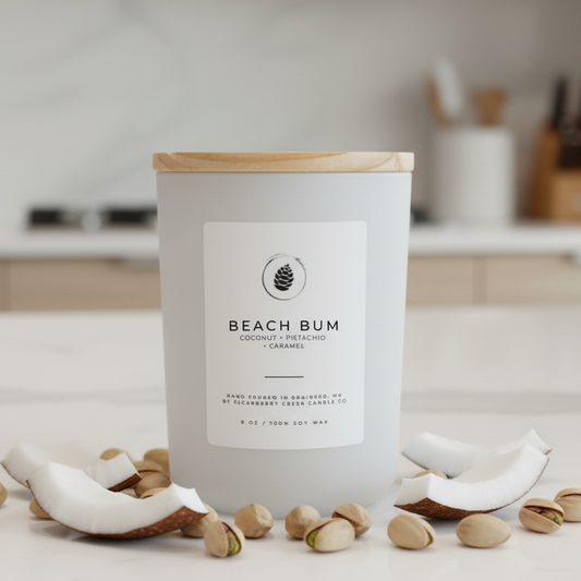 Candle labeled 'Beach Bum' with coconut shells and pistachios on a kitchen counter.