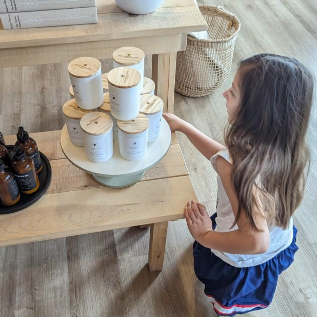 Young girl looking at white candles with wooden lids, stacked on a white pedestal tray