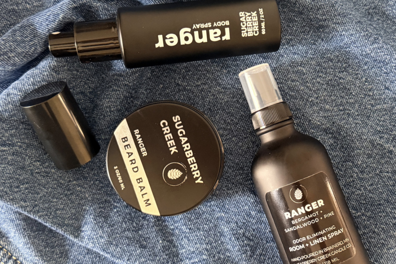 Black beard balm tin, body spray and room spray bottle on a denim surface