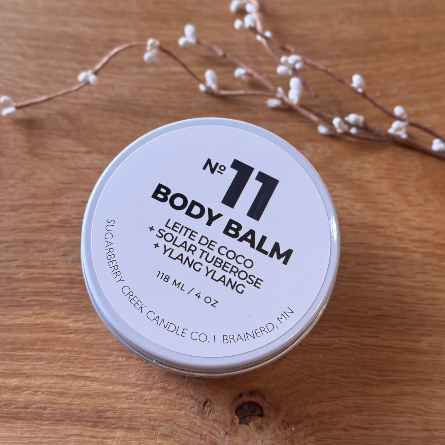 Body balm container labeled 'No. 11' on a wooden surface with decorative elements.