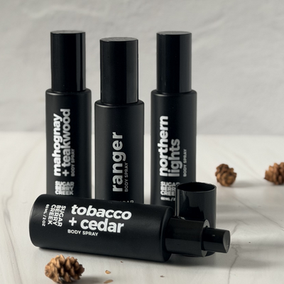 Four black body spray bottles with visible brand names on a light background