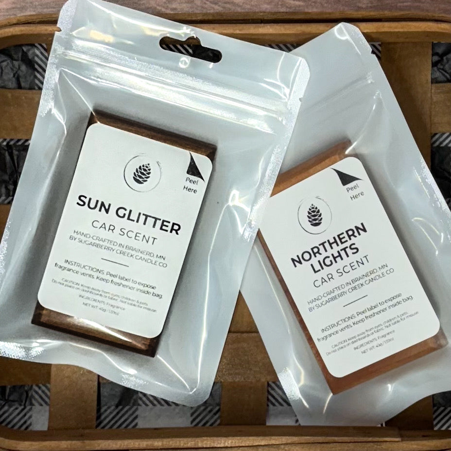 Two car scent packets, 'Sun Glitter' and 'Northern Lights', on a wooden surface.
