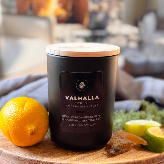 Valhalla candle on a wooden board with fruits and a fireplace in the background
