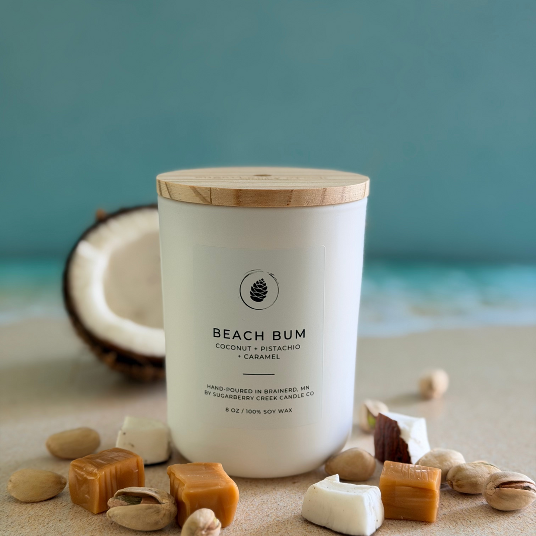 Candle labeled 'Beach Bum' with coconut and candy elements on a sandy background