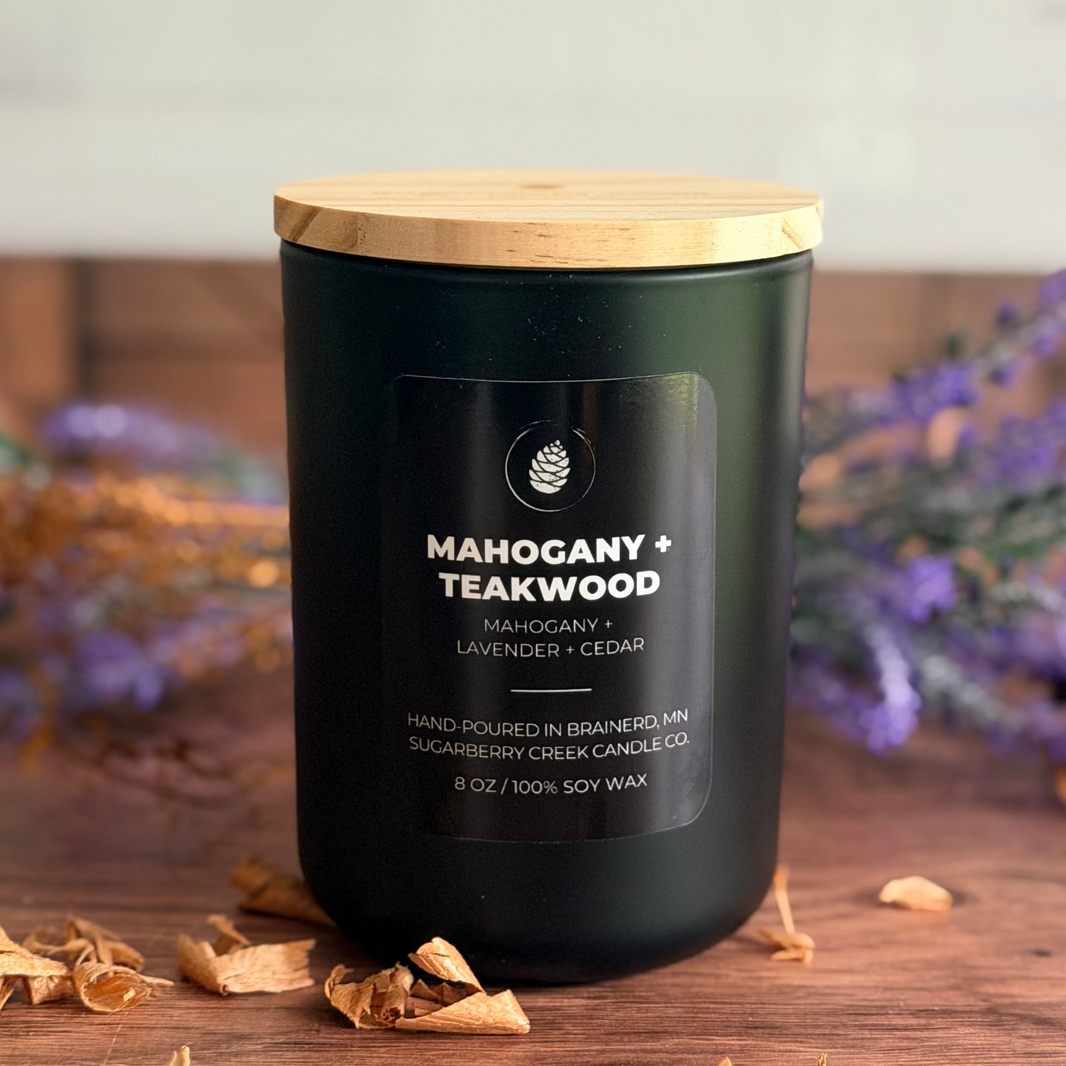 Black candle with wooden lid on a wooden surface with lavender and dried leaves.
