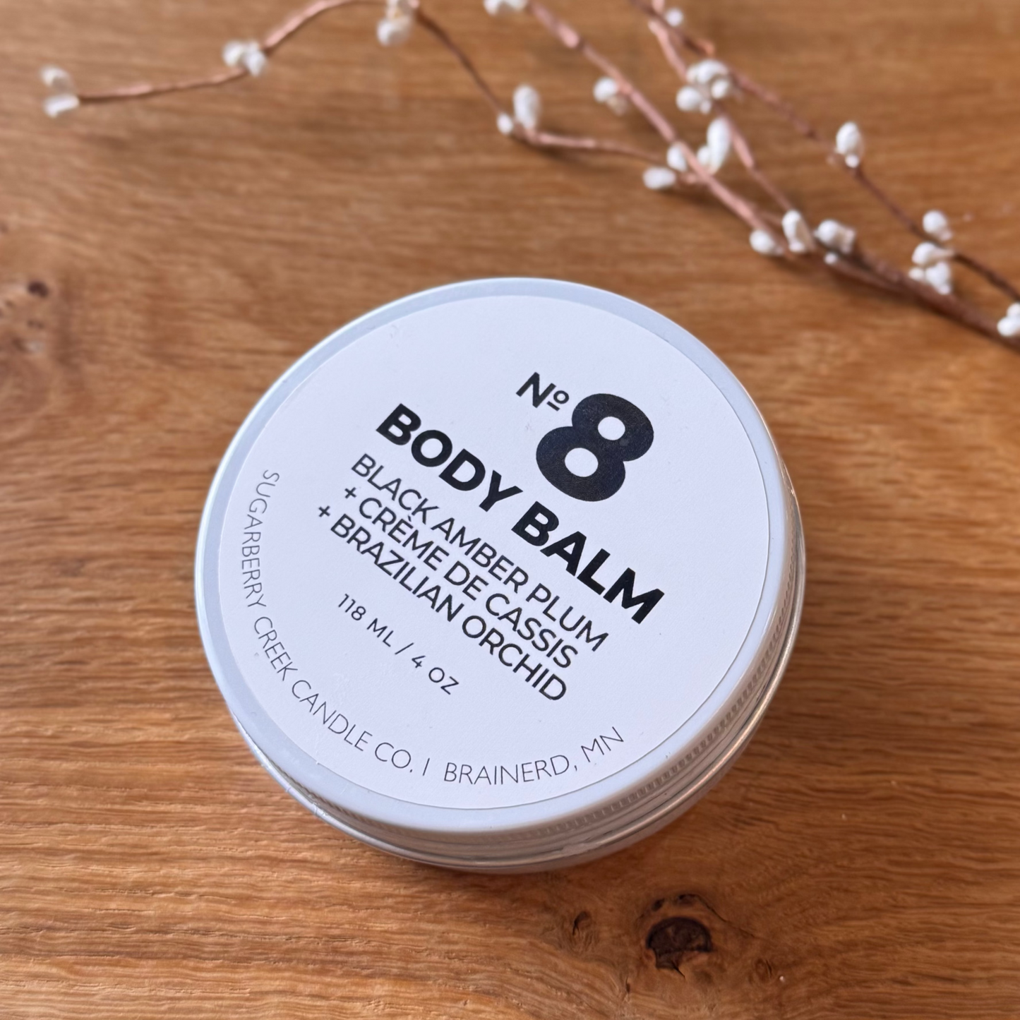 Body balm container labeled 'No. 8' on a wooden surface with decorative branches.