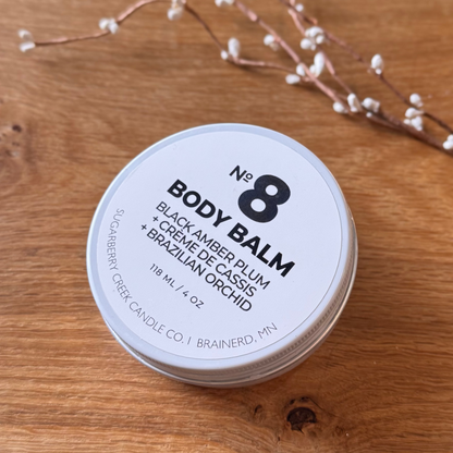 Body balm container labeled 'No. 8' on a wooden surface with decorative branches.