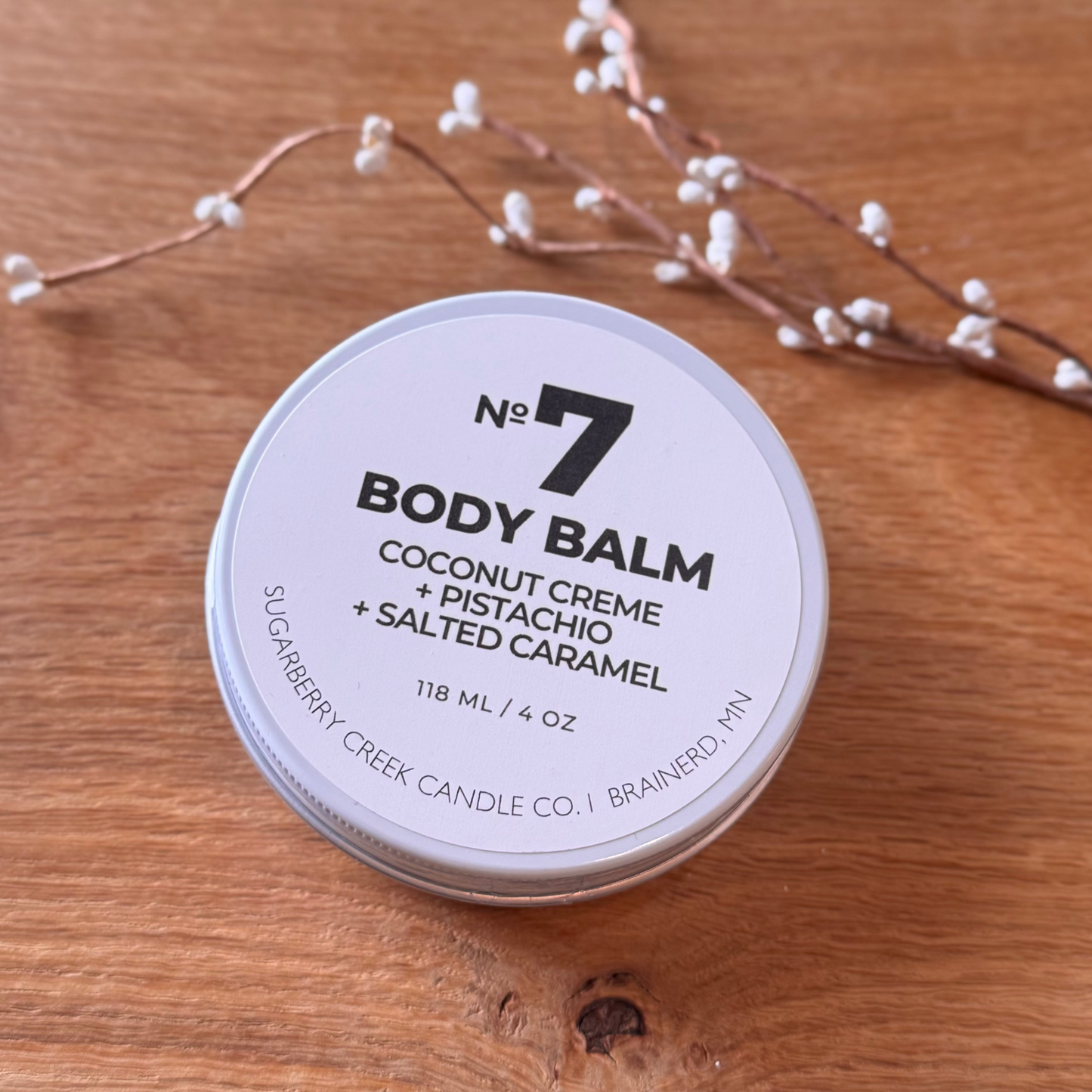 Body balm container labeled 'No. 7' on a wooden surface with decorative branches.