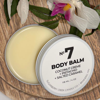 Body balm in a tin with a decorative label on a wooden surface with flowers.