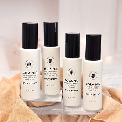 Four bottles of Sola body spray on a white surface with a beige towel.