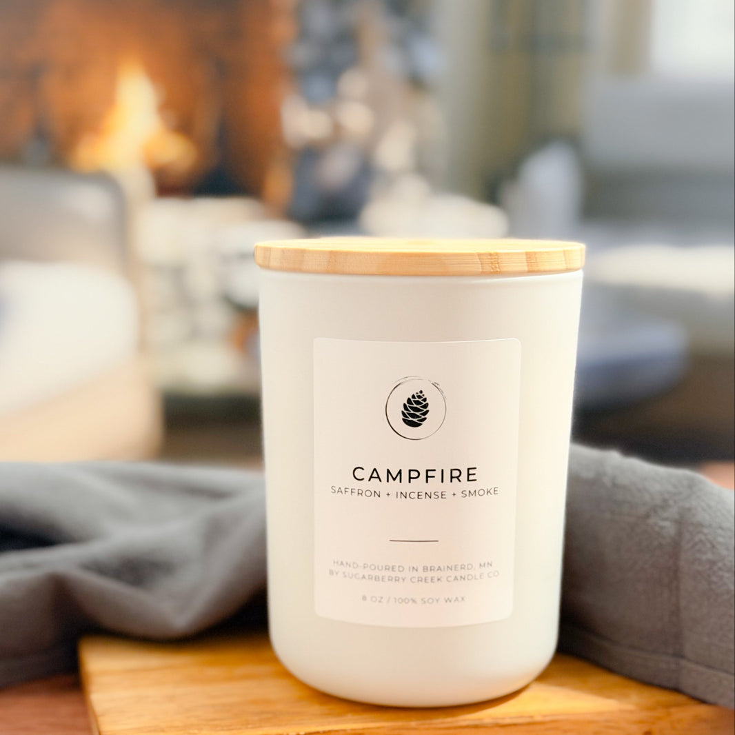 Candle labeled 'Campfire' on a wooden surface with a blurred indoor background