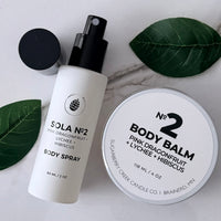 Body spray and body balm with green leaves on a marble surface