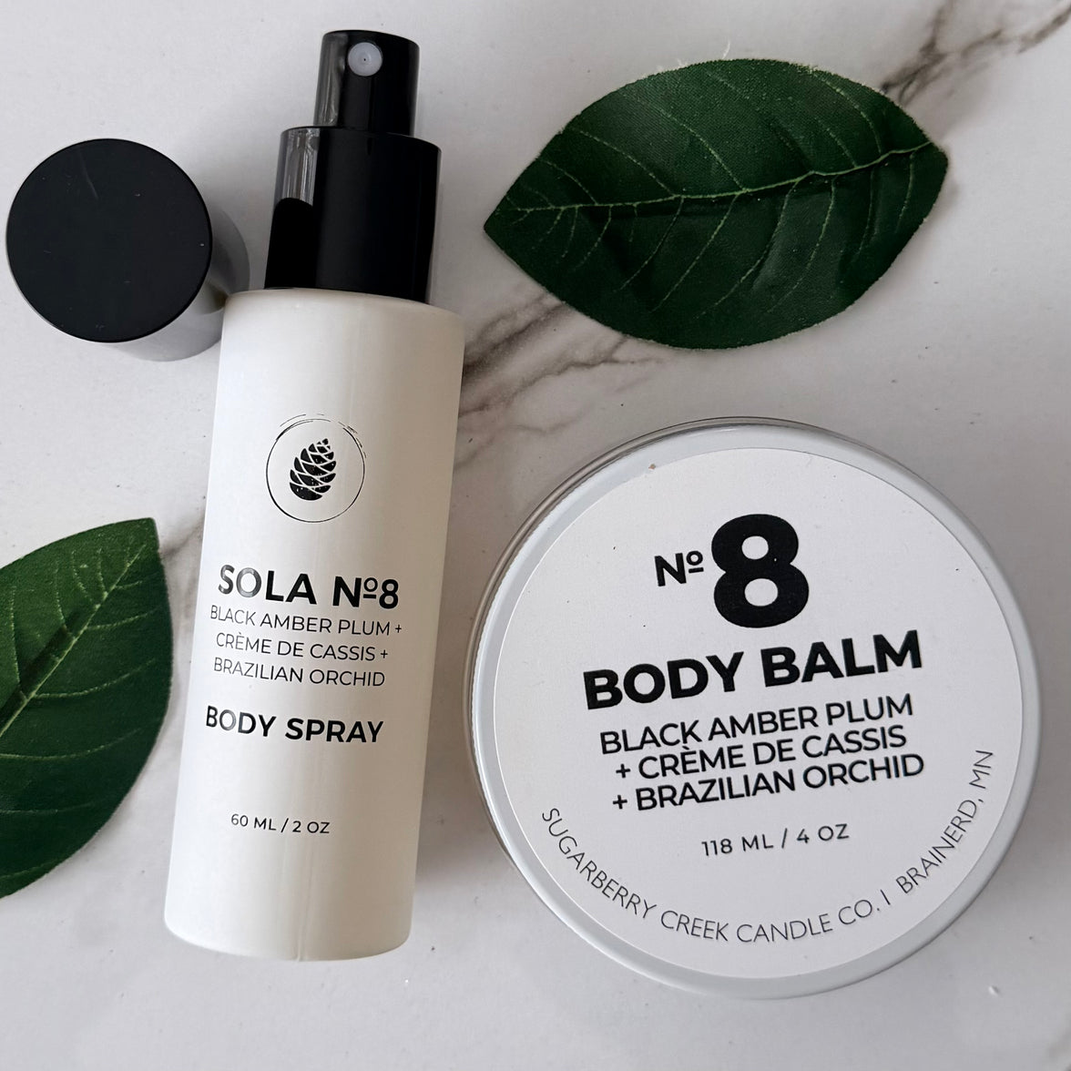 Body spray and body balm with 'Sola No. 8' branding on a marble surface with leaves.