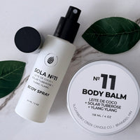 Sola No. 11 body spray and body balm on a marble surface with green leaves.