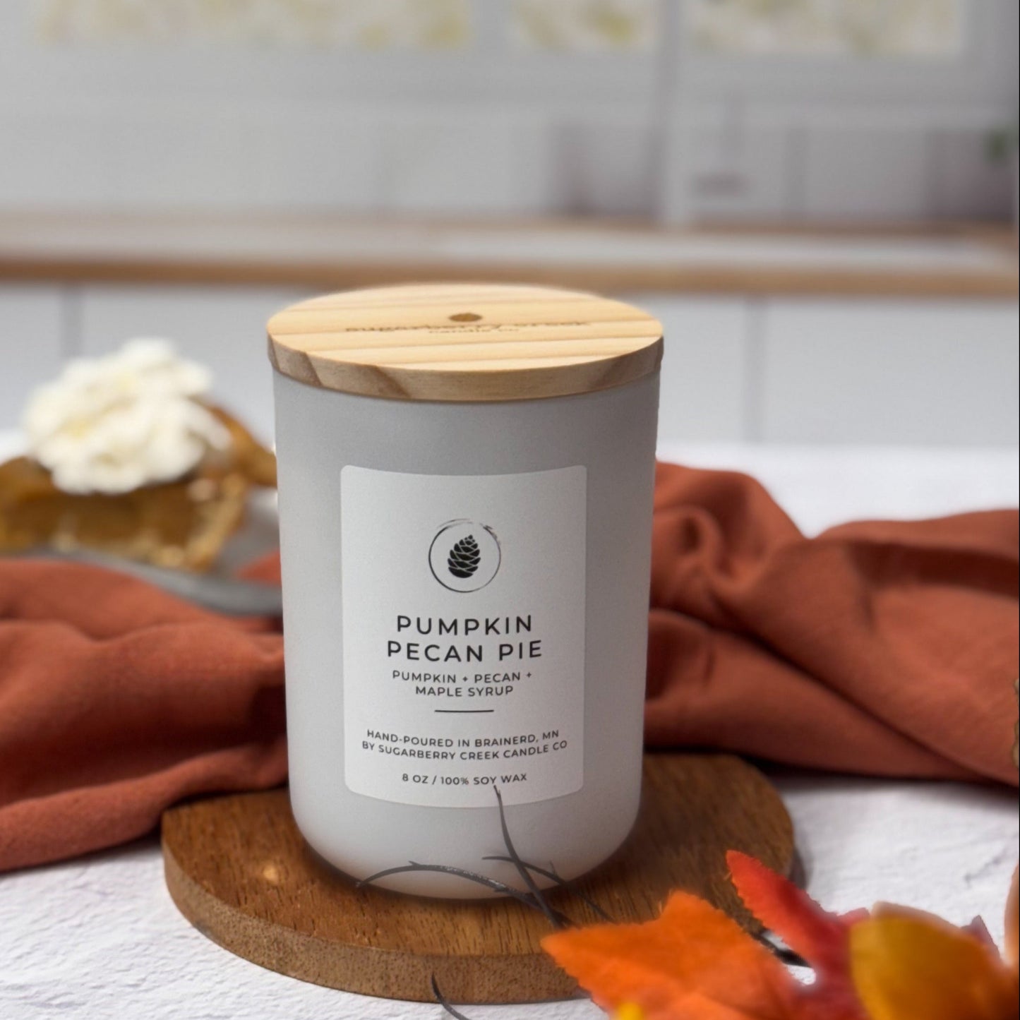 Candle labeled 'Pumpkin Pecan Pie' on a kitchen counter with autumn decorations.