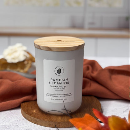 Candle labeled 'Pumpkin Pecan Pie' on a kitchen counter with autumn decorations.